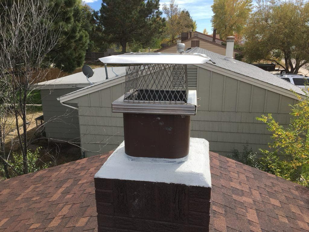 New stainless steel chimney cap with spark screen installed on a Kansas City chimney with a freshly parged white crown