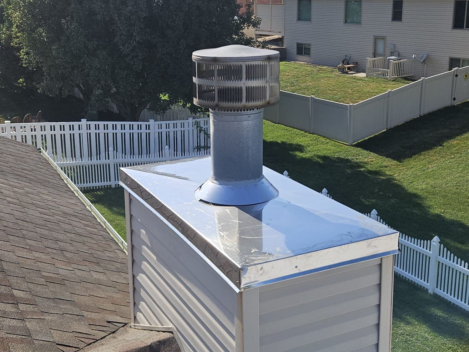 Corner view of the new stainless steel chase cover on the same chimney chase, with the edge lapped over the siding