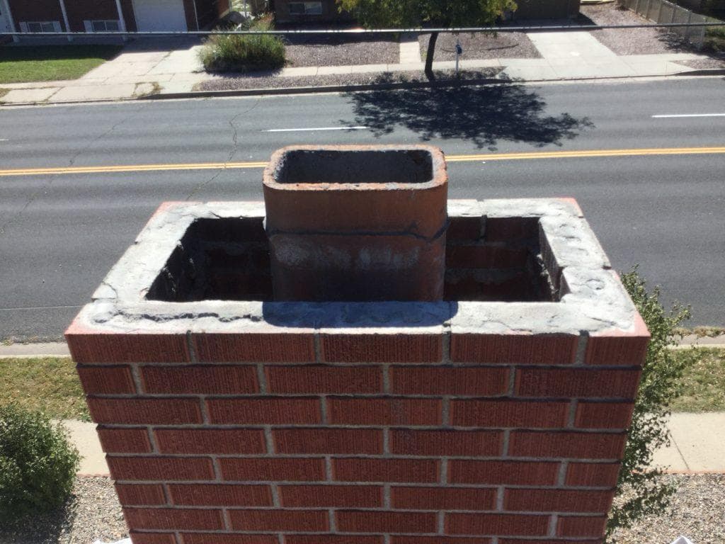 Red brick chimney with the failed crown removed, exposing the clay flue tile and top course of brick mid-rebuild