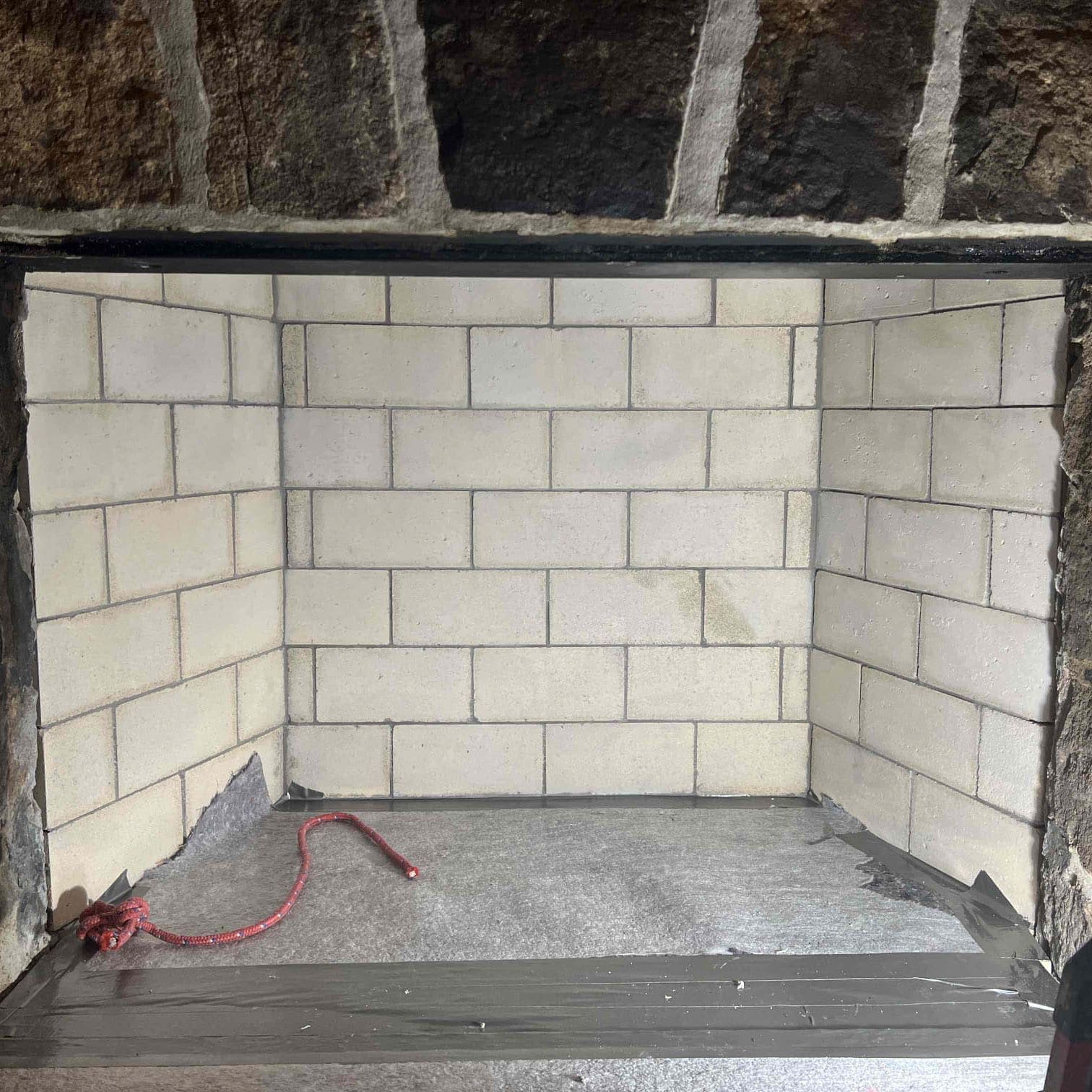 Rebuilt fireplace firebox lined with new firebrick and fresh refractory mortar joints, drop cloth still in place