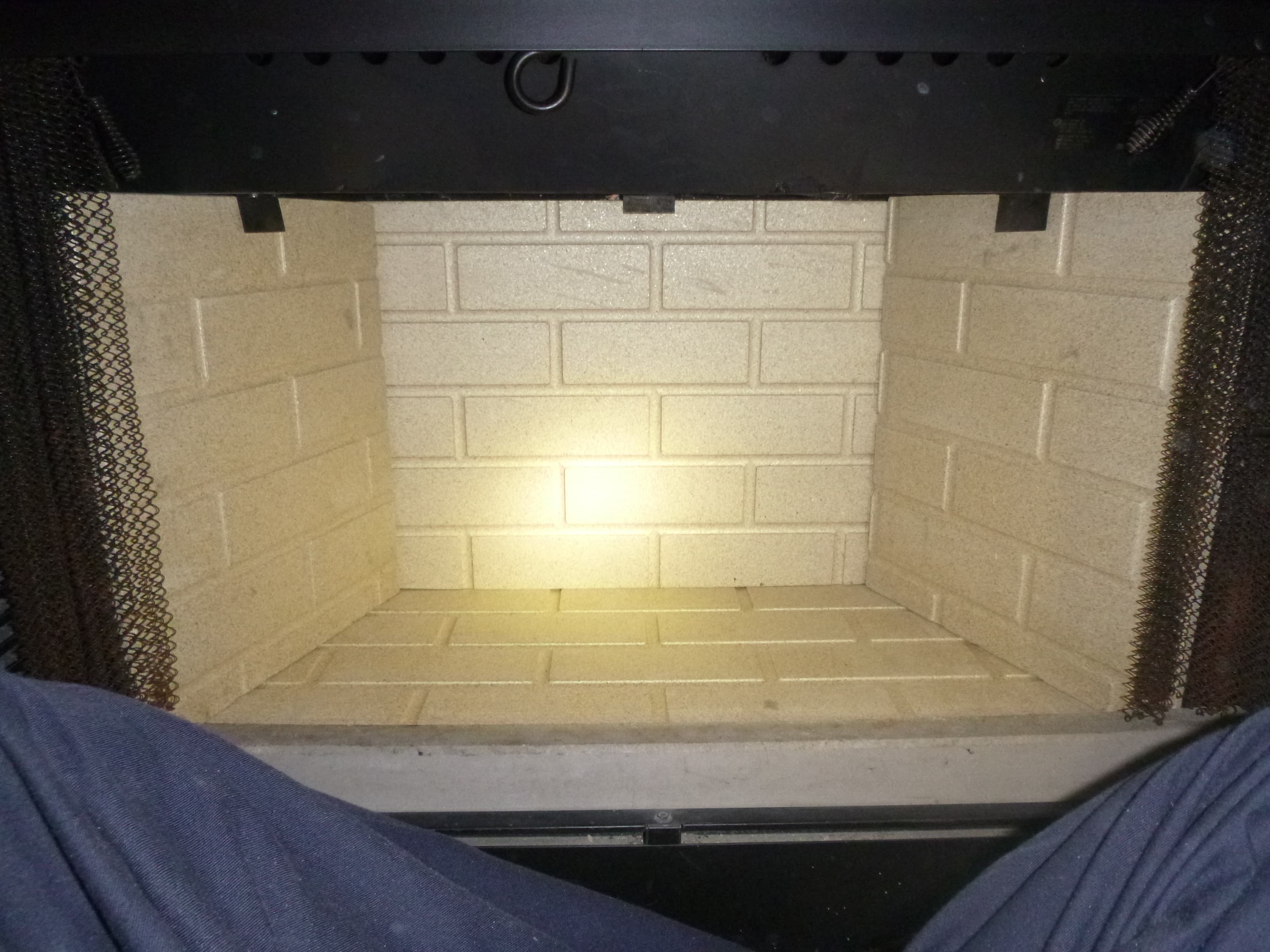 Factory-built fireplace firebox with newly replaced cream refractory panels, mesh curtains drawn back