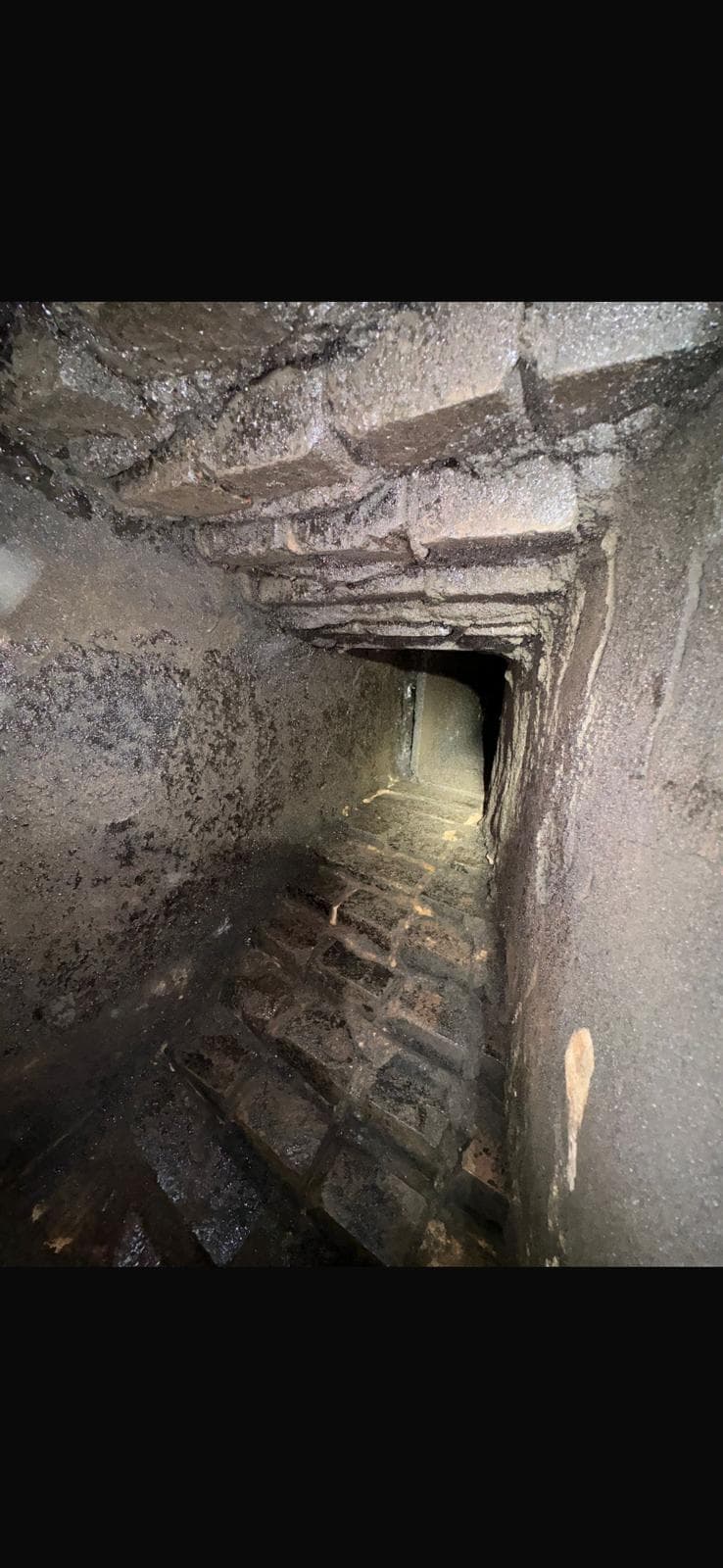 Interior of a sooted, corbelled brick smoke chamber before parging, with heavy creosote deposits on rough brickwork