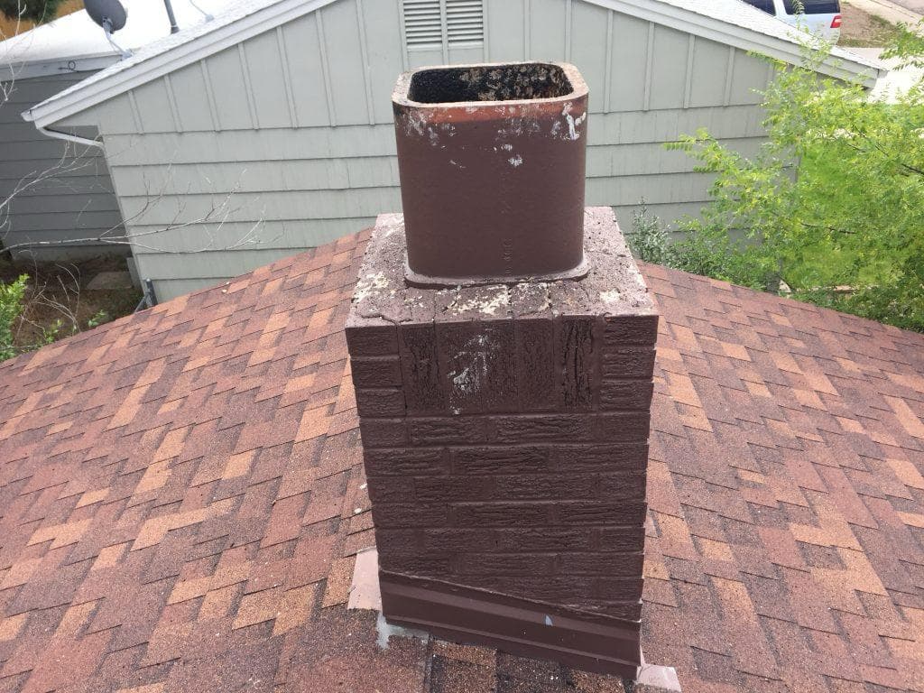 Painted brick chimney with an exposed clay flue tile and no cap, open to rain and animals